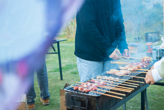 A group of people standing around a grill with food on it